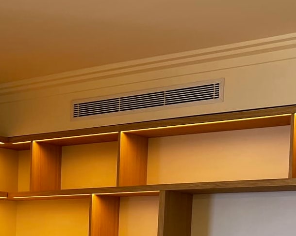 Grille de soufflage d'une climatisation gainable intégrée sous la corniche, au-dessus d'une bibliothèque en chêne