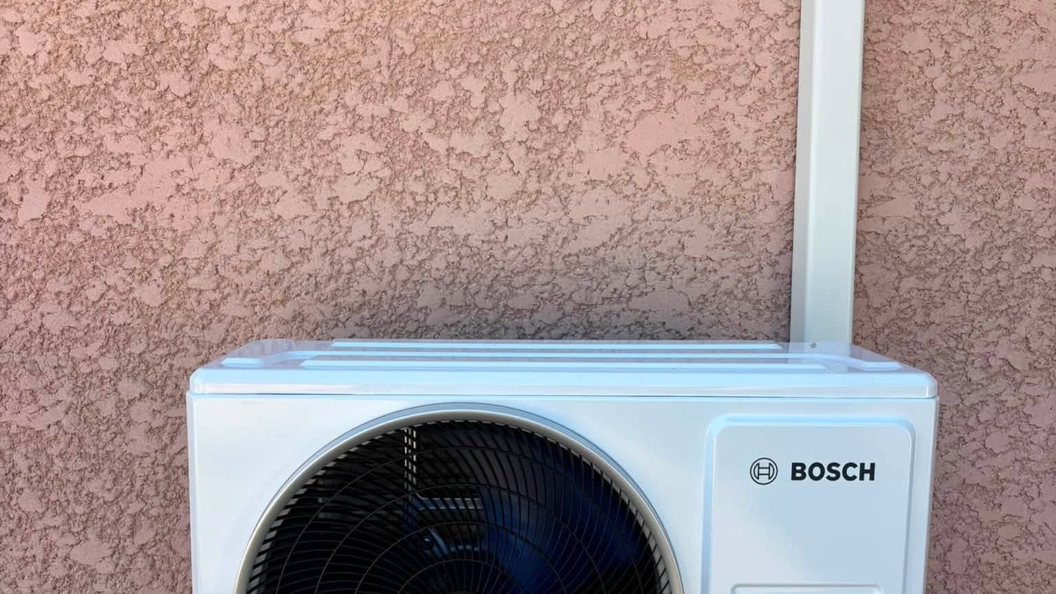 Groupe extérieur de climatisation fixé sur un mur crépi, vue de face