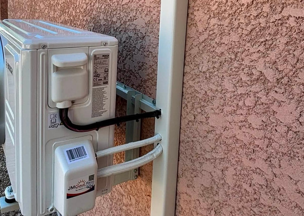 Groupe extérieur de climatisation posé sur une façade crépi, oliviers en arrière-plan