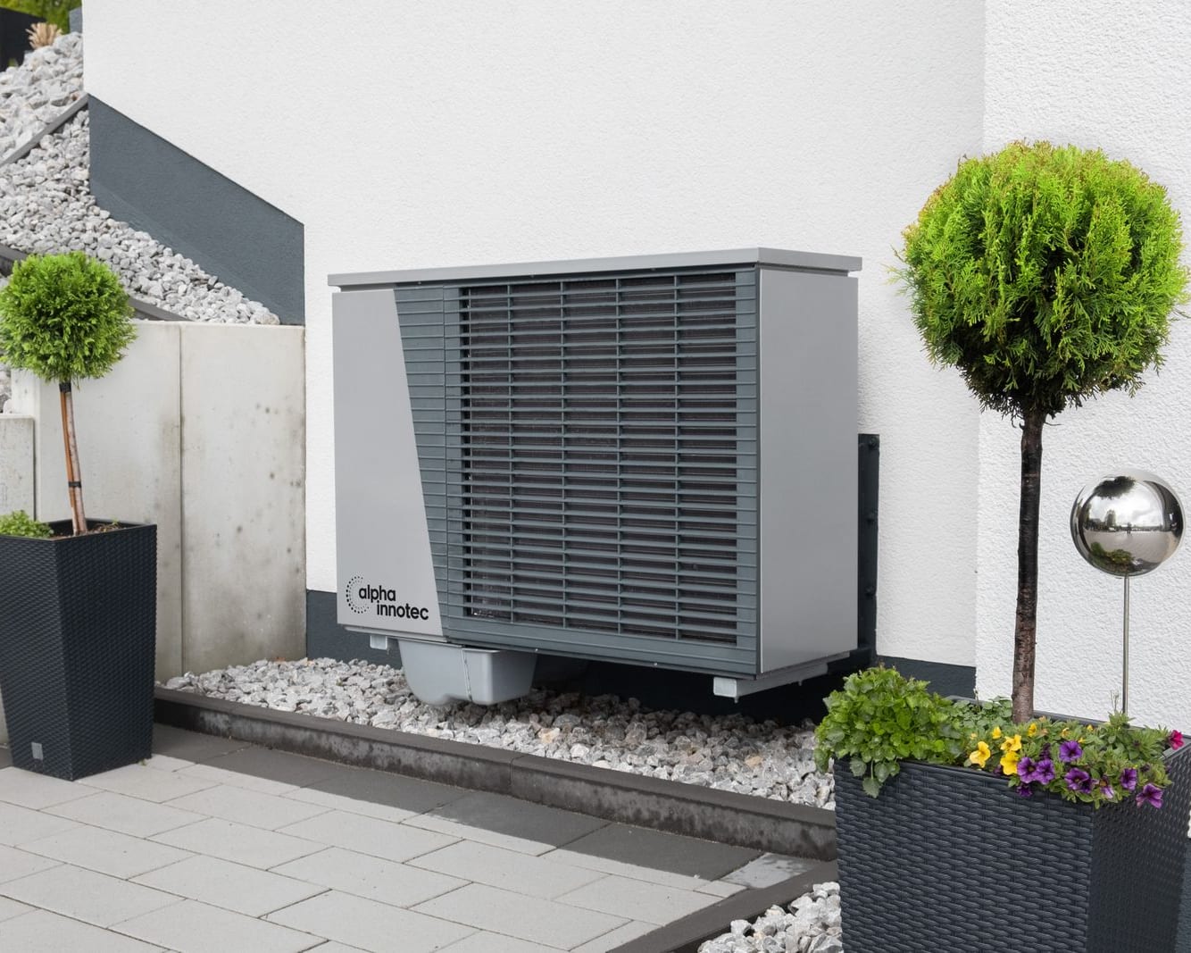 Pompe à chaleur air-eau murale installée devant une maison, entre deux jardinières